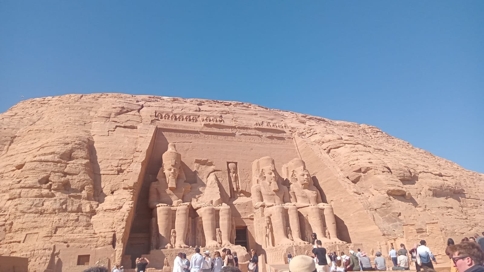 Great Temple of Ramesses II at Abu Simbel, Egypt, with four colossal seated statues carved into the sandstone cliff and tourists at the entrance